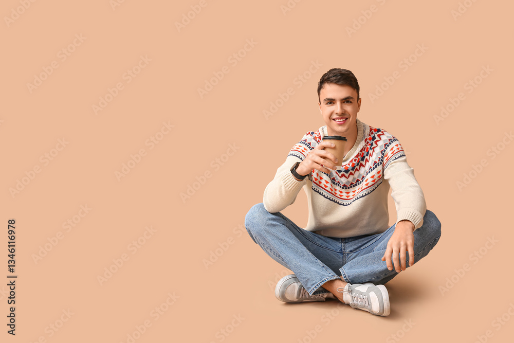 Handsome young man in stylish sweater with paper cup of hot coffee sitting on brown background Handsome young man in stylish sweater with paper cup of hot coffee sitting on brown background