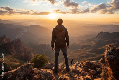 A man stands at peak of a mountain, basking in warm glow of setting sun, overlooking a vast expanse below, feeling accomplished and connected to natural world