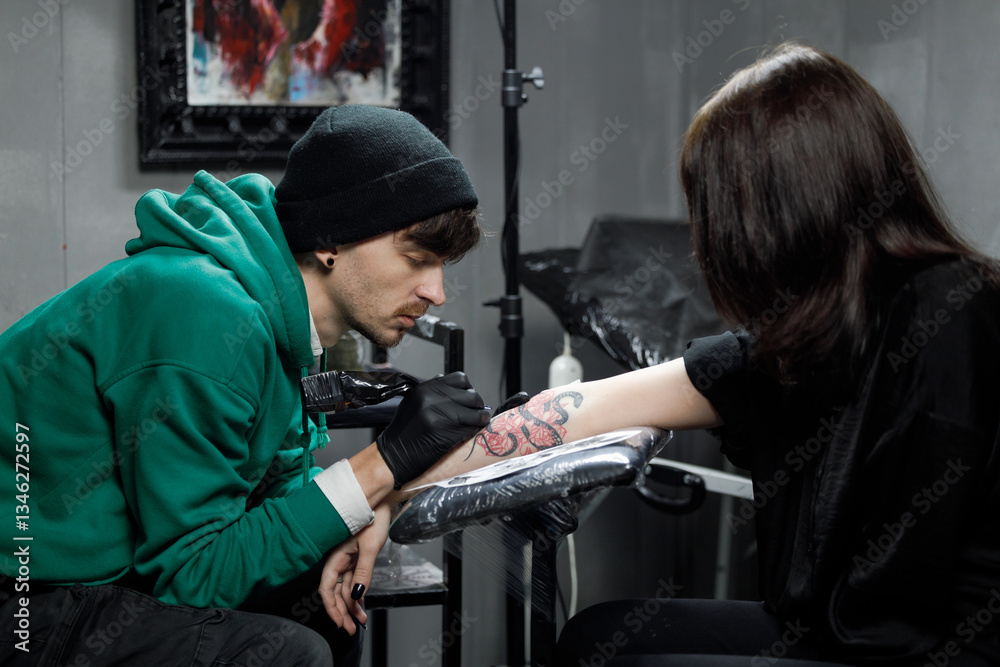 Obraz premium Close up tattoo master professional tattoo artist in black gloves making a rose tattoo on a man's forearm. He is holding a tattoo machine.