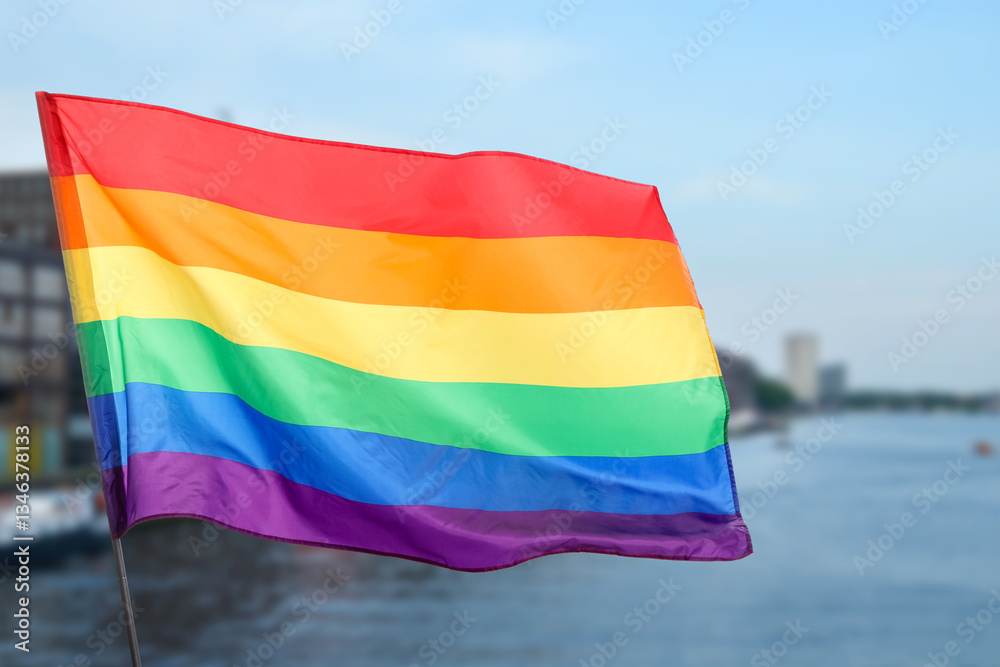 Obraz premium LGBT flag fluttering in city near river, selective focus