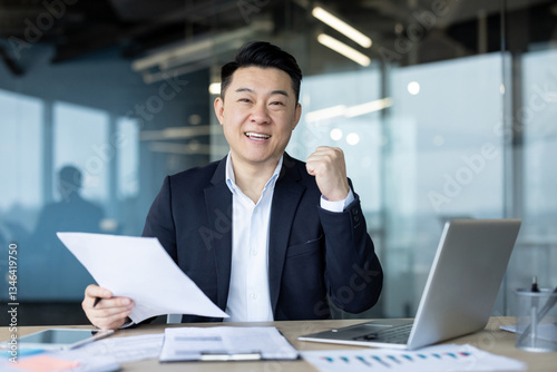 Fotografi Portrait of a young cheerful Asian businessman sitting in the office at his desk
