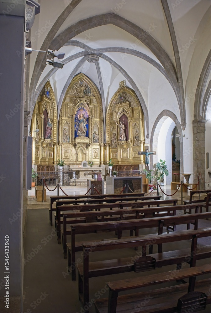 Fototapeta premium Santa Pau, Spain - Feb 24, 2025: Church Santa Maria. Walking in Santa Pau suburb. Streets, buildings. Lifestyle in the urban area. Cloudy winter day. Selective focus