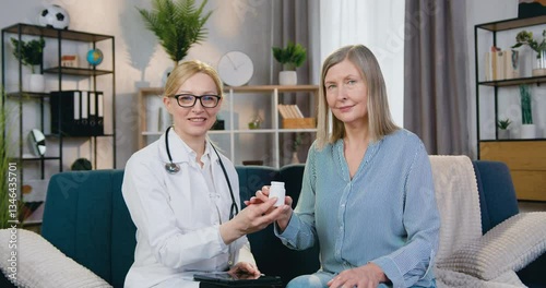 Women doctor and patient sitting in front of camera with sincerely smiles and holding bottle with vitamins. Healthcare concept