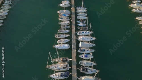 A beautiful aerial video capturing a symmetrical view of sailboats neatly docked along both sides of a central pier in a tranquil marina. 