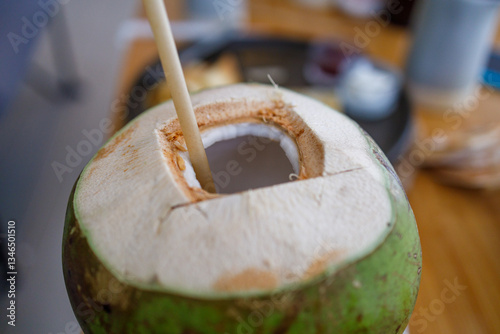 Fresh green coconut with a paper straw inserted into the opening. Close-up view of the white coconut meat and clear coconut water inside
