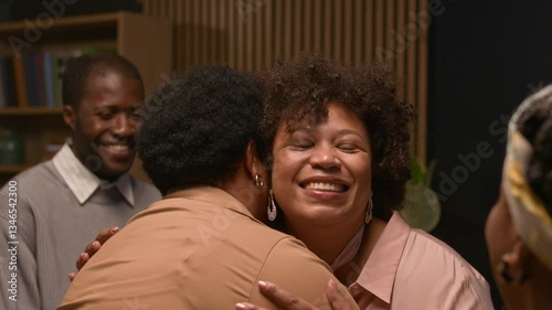 Joyful adult daughter greeting senior mother with gentle hug during festive gathering of whole extended family in living room, happy family moment