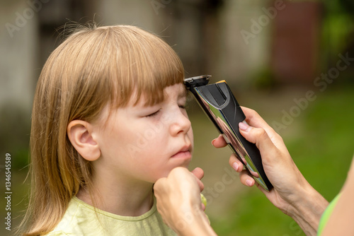 Mother cutting her daughter's hair with electric trimmer outdoors, simple haircut at home, frugal lifestyle, important parenting skills DIY hair cutting, family bonding, natural background, two people