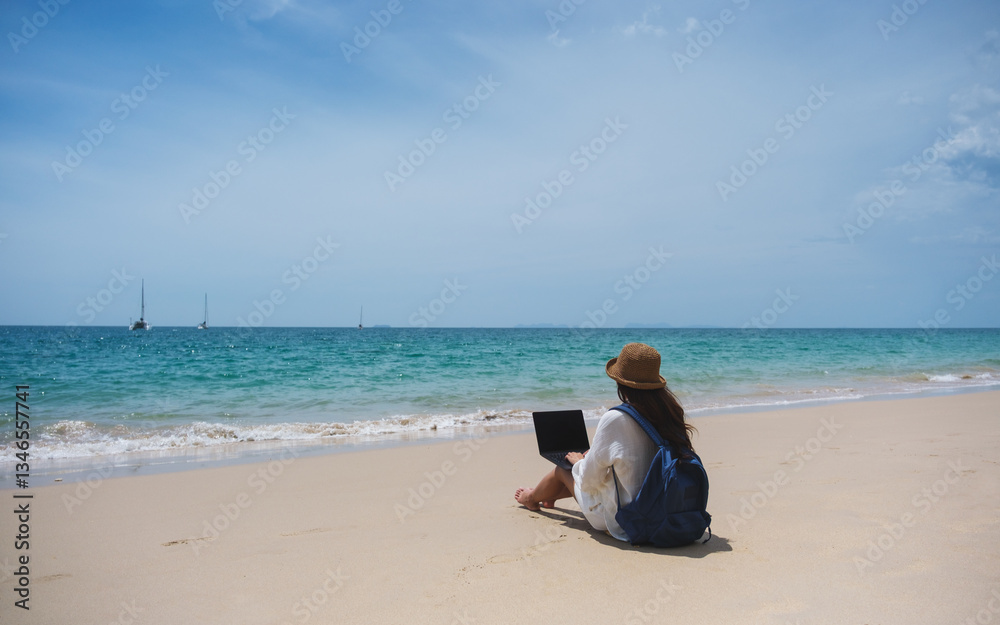 A female traveler using and working on laptop computer while sitting on the beach A female traveler using and working on laptop computer while sitting on the beach