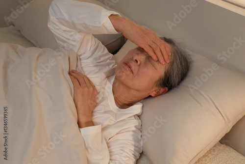 침실 침대에 누워 두통을 느끼는 여성 어르신 - 불면증