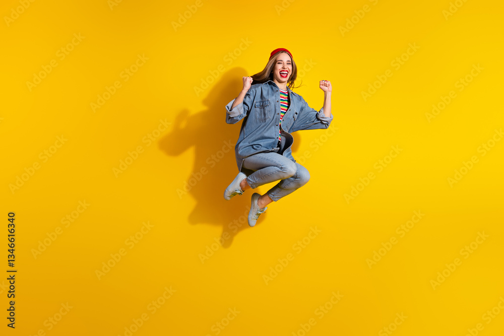 Smiling young woman in denim jumps with excitement on yellow background demonstrating energy and joy Smiling young woman in denim jumps with excitement on yellow background demonstrating energy and joy