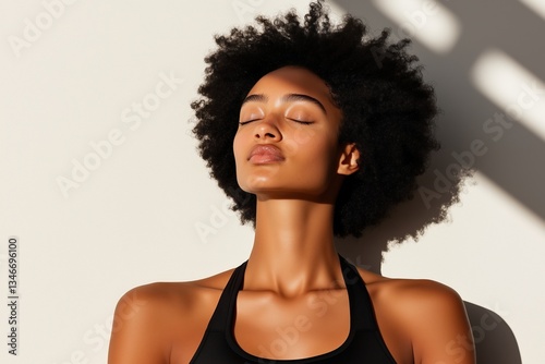 A black woman enjoying sunlight with eyes closed, exuding peace. Her face is bathed in natural light, highlighting her features