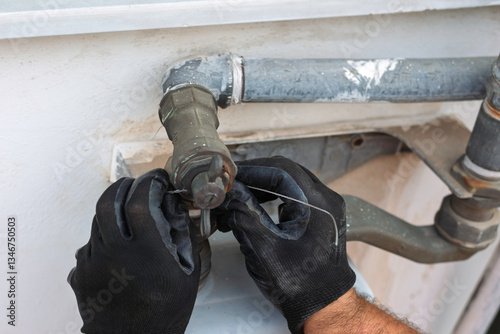 Gas pipe repair with worker using wire to secure a connection. Close-up on hands and tools, highlighting the precision and safety measures. Illustrates plumbing, maintenance, and gas line repair.