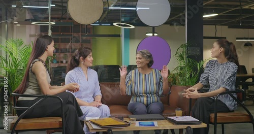 Indian young adult woman talk gossip with old aged boss ceo lady enjoy day spend time job place happy female girl staff team speak share new work deal good news do hand shake show thumbs up at office