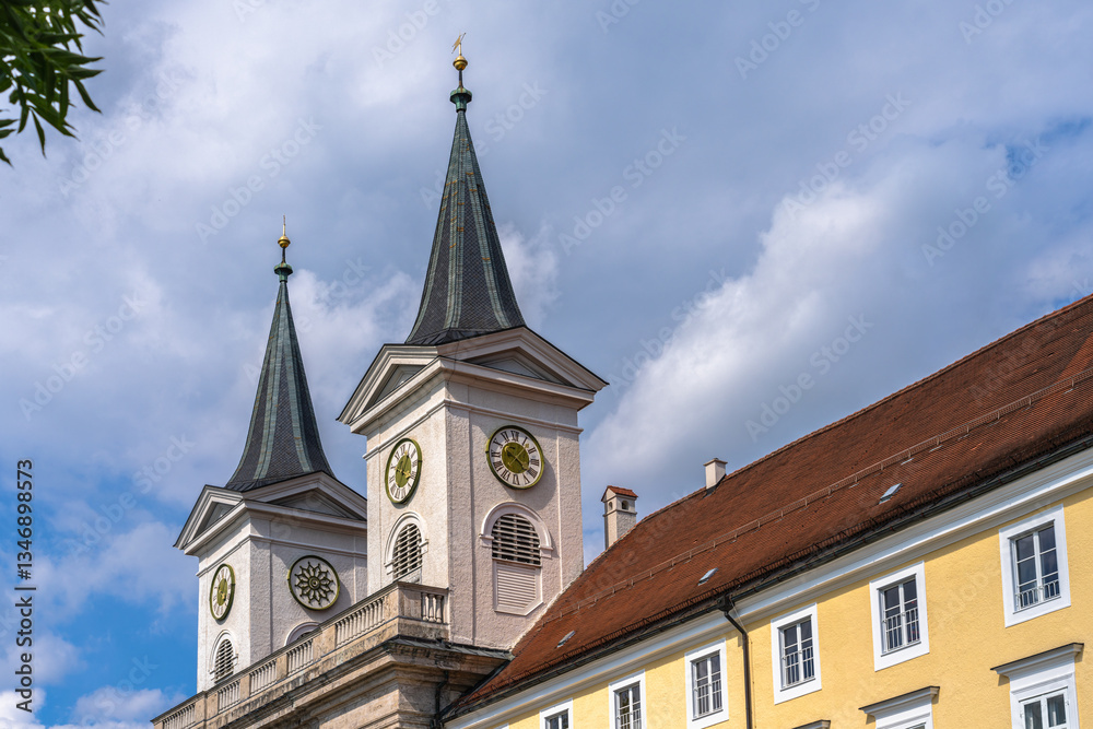 Obraz premium Close view of the double clock towers of St. Quirinus parish church in center of Tegernsee town on a sunny summer day with blue sky cloud, Bavaria, Germany