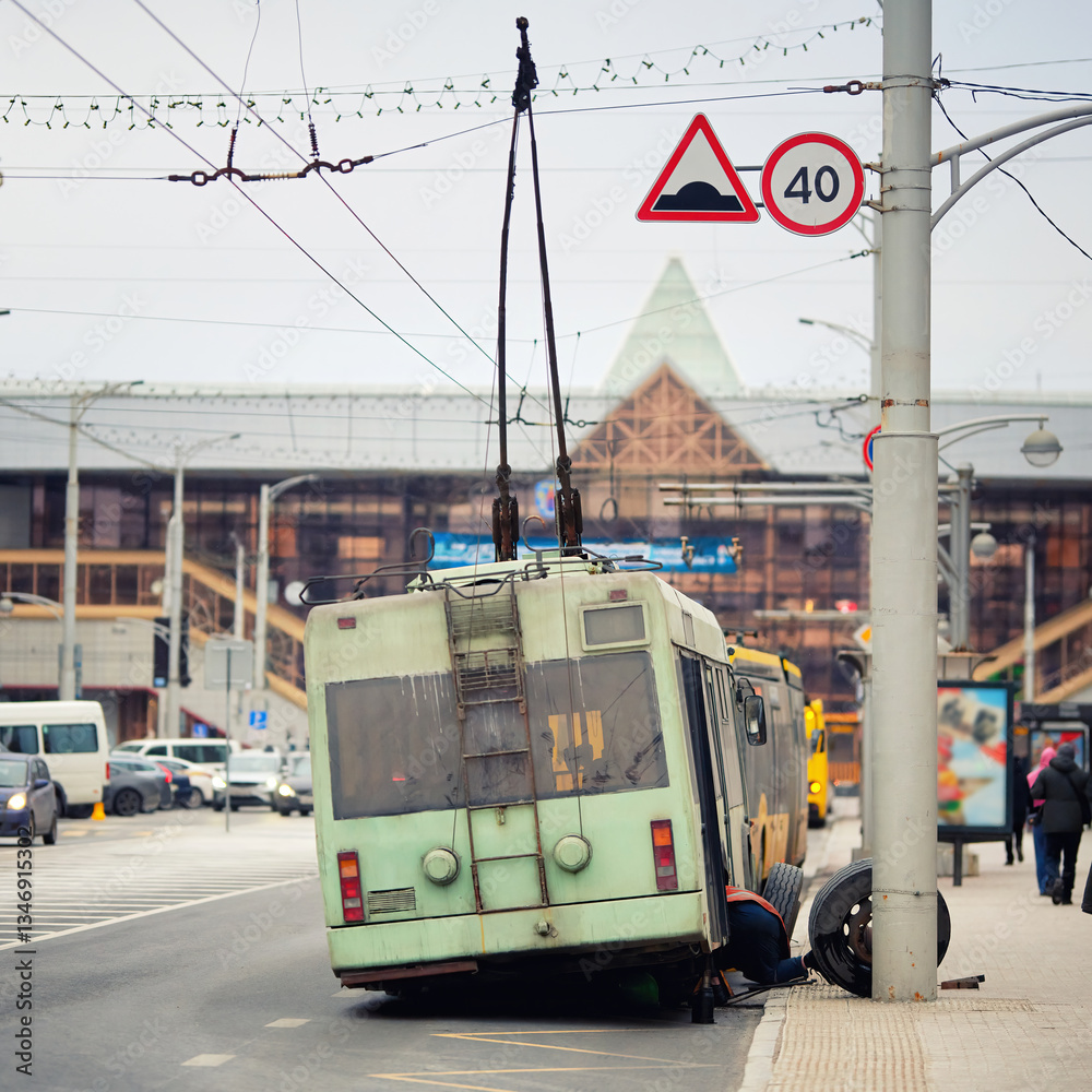 City trolleybus undergoing emergency tire replacement and repair work, lifted on jack on the roadside. Damaged trolleybus with its wheel removed, process of public transport repair, mechanical service