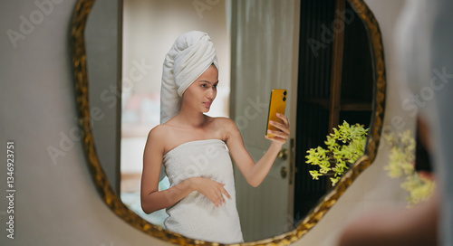Photography Indian happy gen z young adult female lady wrapped towel head and body use mobil