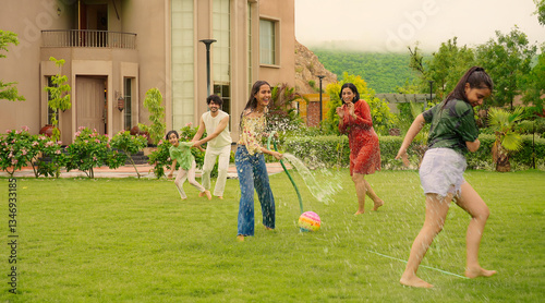Quadro su tela Indian happy teen girl lady mom hold hose pipe spray water on family group play
