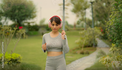Indian young adult gen z relax sports woman lady wear headphone running in fresh air outdoor garden park sporty teen girl do self body care warm up learn good health habit daily life enjoy day time