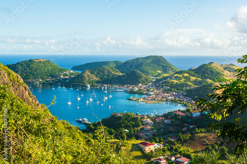 Vue de haut de la baie des Saintes en Guadeloupe avec la mer des Caraïbes, l'île de Terre de Haut, et des bateaux par une journée ensoleillée avec des nuages.