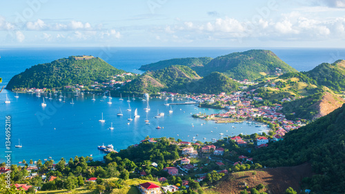 Vue de haut de la baie des Saintes en Guadeloupe avec la mer des Caraïbes, l'île de Terre de Haut, et des bateaux par une journée ensoleillée avec des nuages.