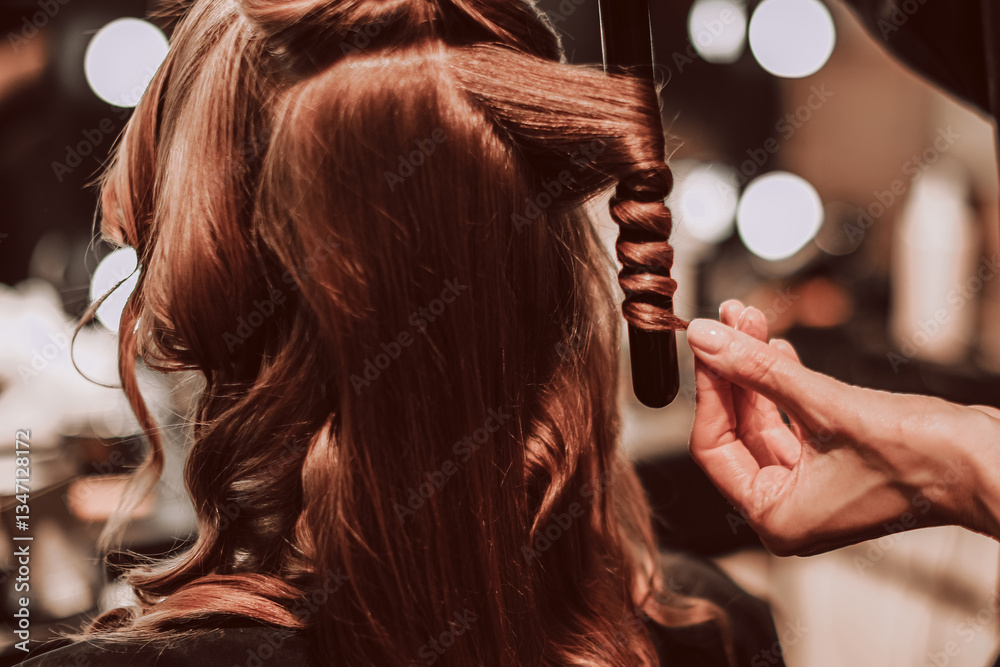 Naklejka premium Female hands of a stylist doing a hairstyle of a young fashion model, back view