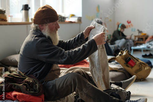 Bilde på lerret Side view of senior male refugee with long grey beard sitting on his sleeper and