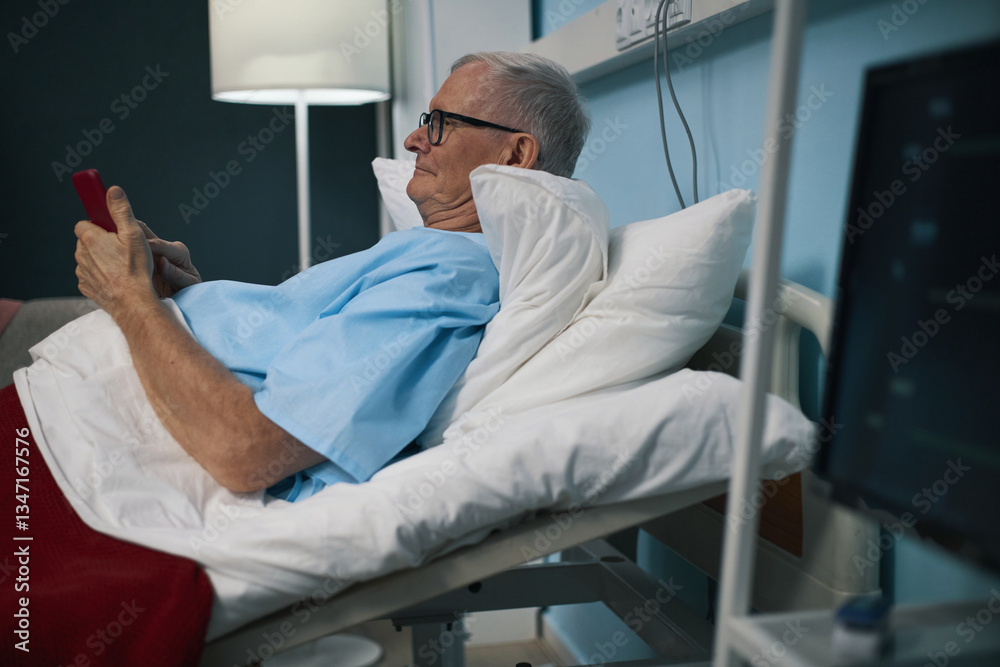 Senior man lying on bed in the ward and using his smartphone Senior man lying on bed in the ward and using his smartphone