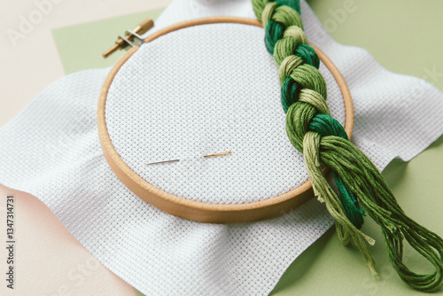 Embroidery tools wooden hoop, green embroidery floss, and needles on white fabric, arranged for needlework and crafting, cross stitch concept