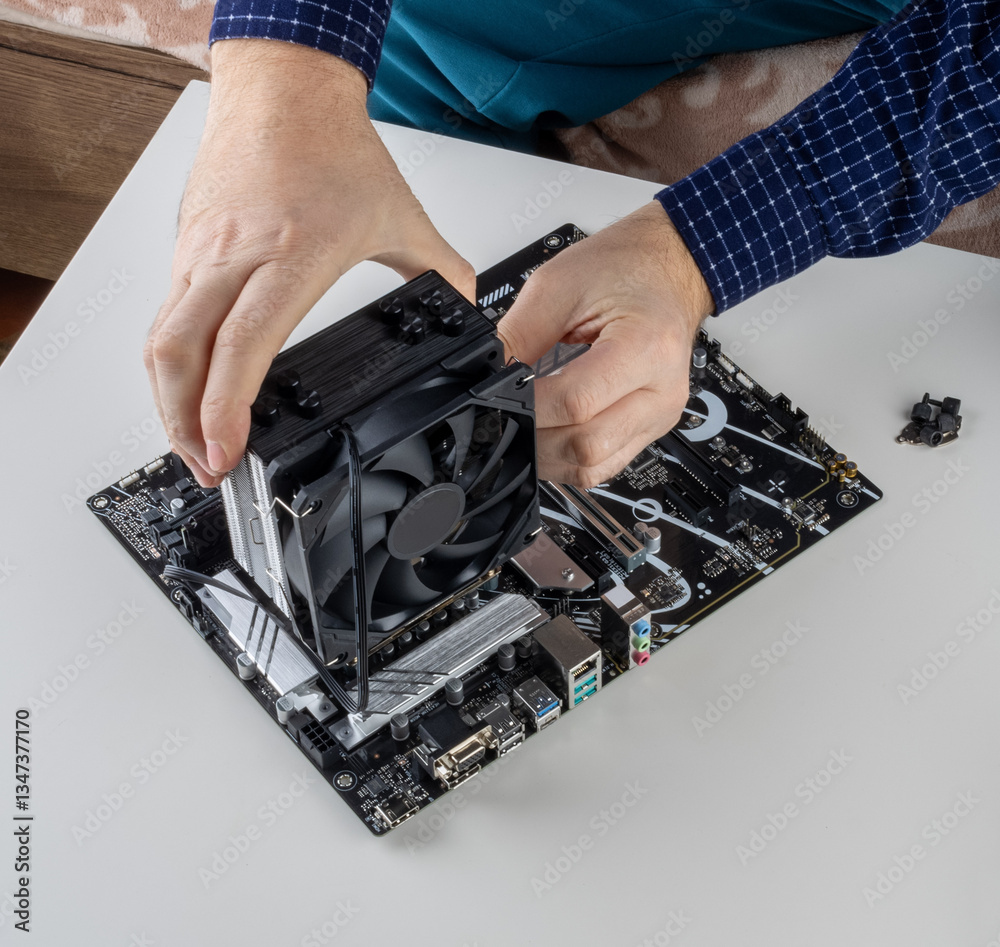 the hands of a man installing a fan on the CPU cooler tower on the motherboard