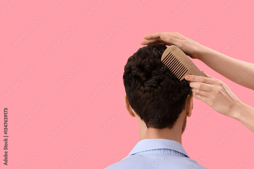 Fototapeta premium Female hairdresser combing hair of young man on pink background, back view
