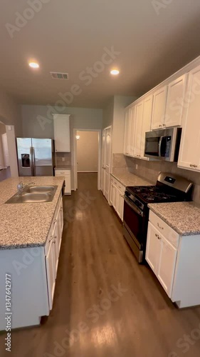 Empty american house kitchen with white cabinets granite countertops wood floors and stainless steel appliances in open concept design. 