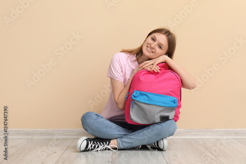 Smiling young female student with pink backpack sitting on floor, back to sch...