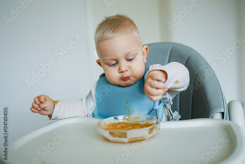 A cute little baby is having a delightful time during their mealtime while seated in a high chair, joyfully making a fun and messy experience with a tasty snack that they are enjoying