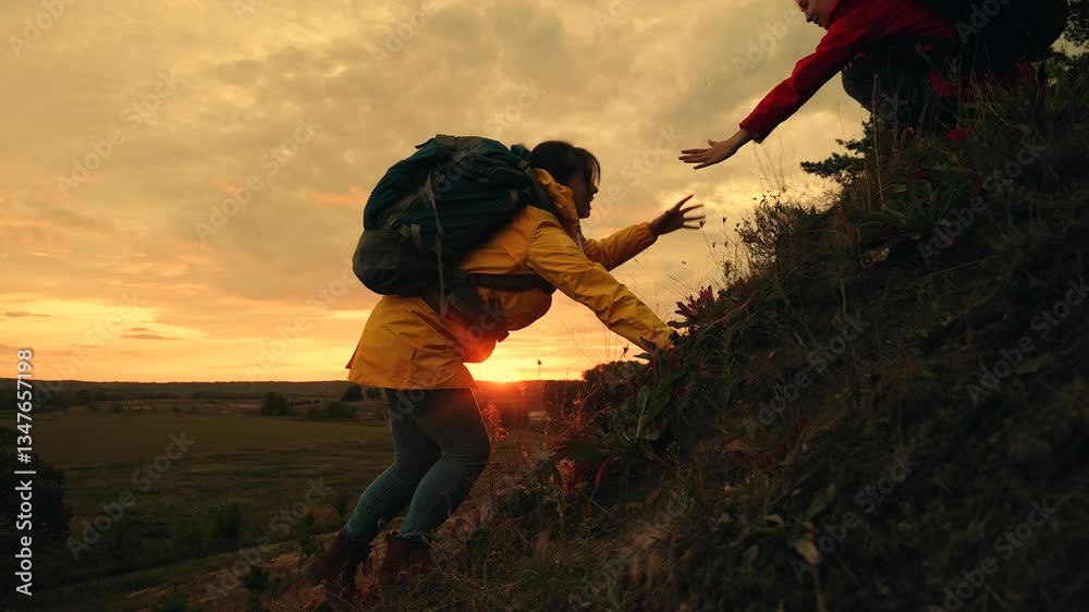 Tired woman with backpack climbs on steep hill top with friend help in autumn park at sunset. Strong woman takes friend helping hand to reach hill top together. Women practice mountain climbing