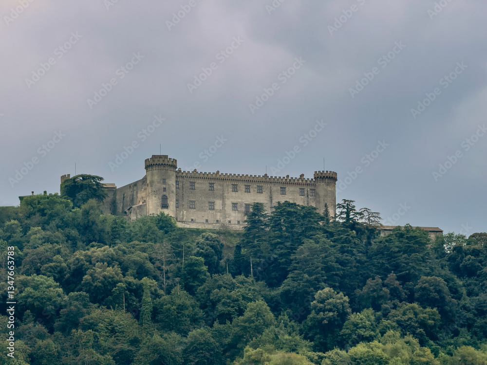 Lake Bracciano, Lazio, Italy - July 7, 2024: Fortress, Castello Orsini-Odescalchi, on hill above the lake. Forest on the hill under cloudscape