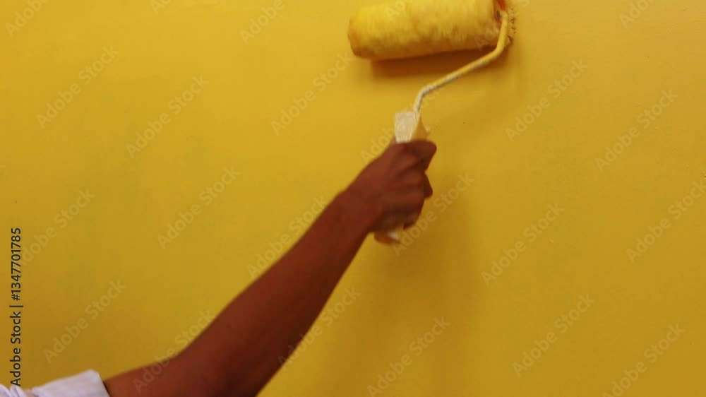Wall painting activity or painting the wall with yellow color using paint roller. Concept of self-repair and home construction concept.