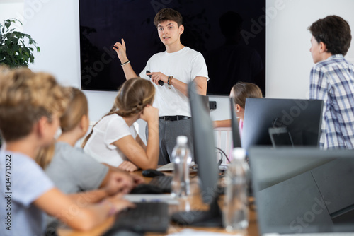 Young computer science teacher standing near an interactive whiteboard tells new material to teenage students in a school computer class