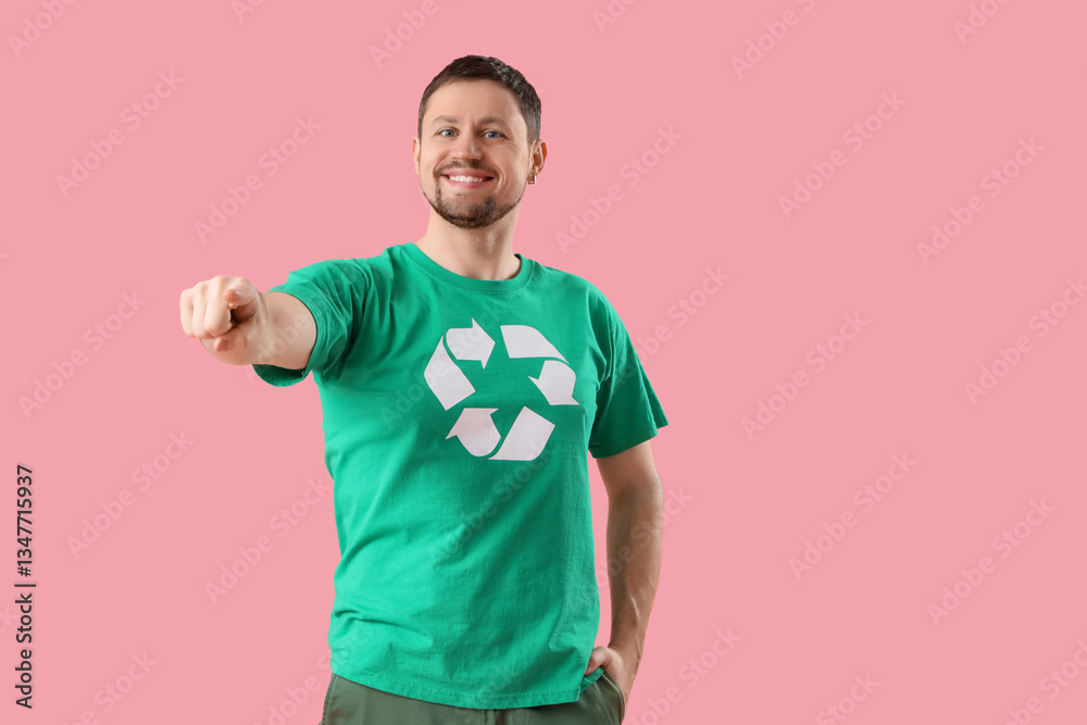 Happy young man in t-shirt with recycling logo pointing at viewer on pink background. Ecology concept Happy young man in t-shirt with recycling logo pointing at viewer on pink background. Ecology concept
