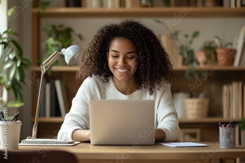 A woman is seated at a desk, utilizing a computer and simultaneously writing in a notebook