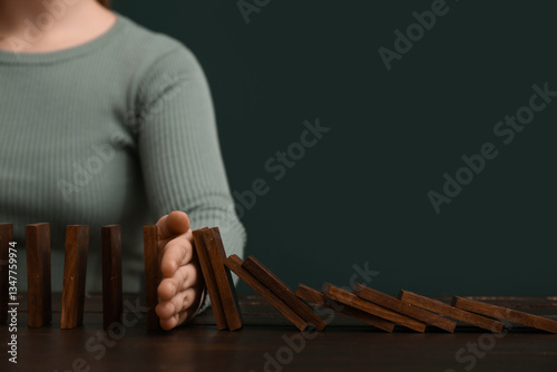 Tablou pe pânză Woman stopping domino effect at black wooden table