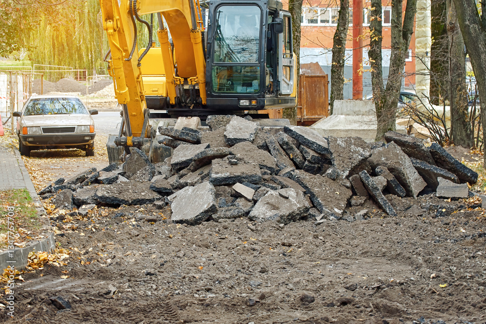 Excavator at district construction site engaged in infrastructure renovation, digging and moving broken asphalt pavement to lay pipes and prepare roads for modern urban development