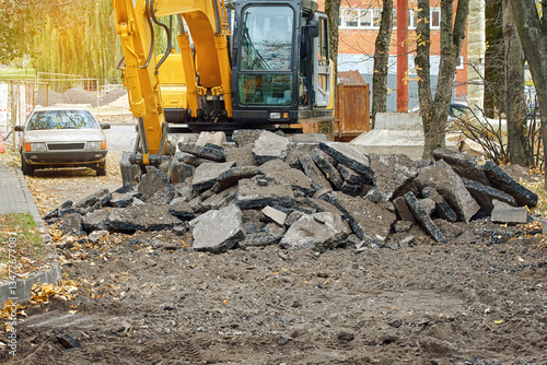 Excavator at district construction site engaged in infrastructure renovation, digging and moving broken asphalt pavement to lay pipes and prepare roads for modern urban development