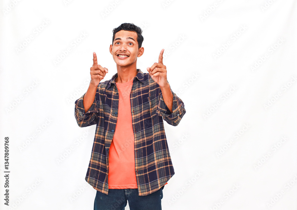 Enthusiastic young man joyfully pointing upwards on a clean white backdrop Enthusiastic young man joyfully pointing upwards on a clean white backdrop