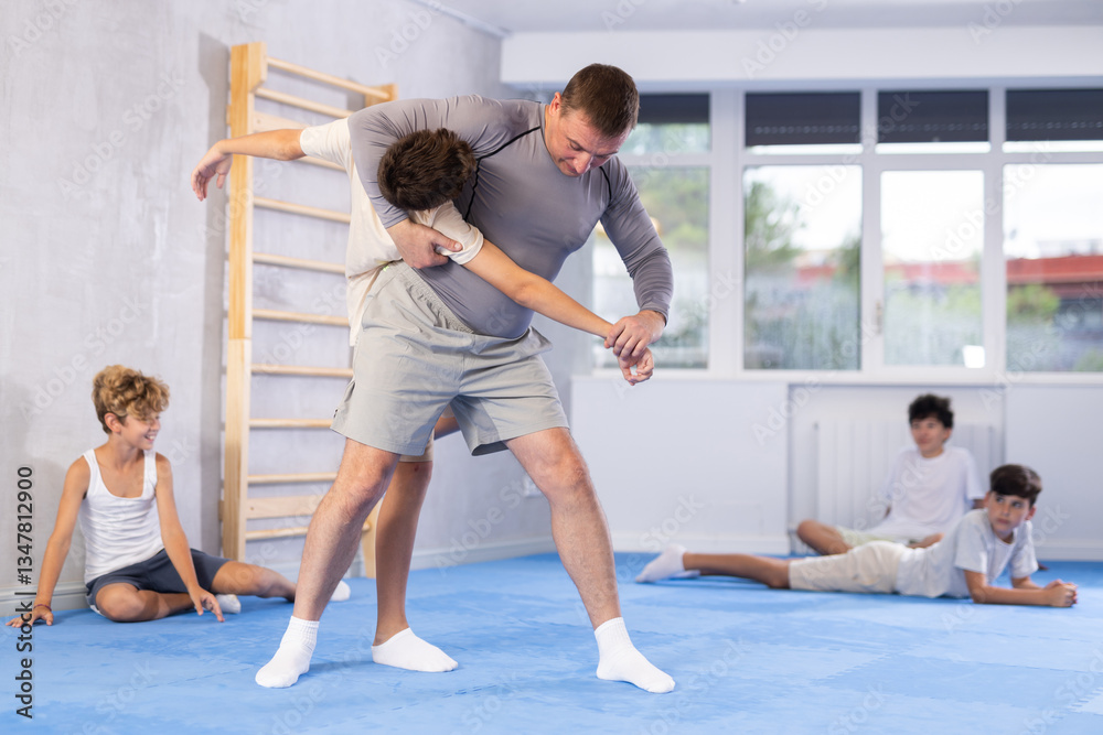 Experienced middle-aged teacher conducting training with preteen attendees of self-defense classes Experienced middle-aged teacher conducting training with preteen attendees of self-defense classes