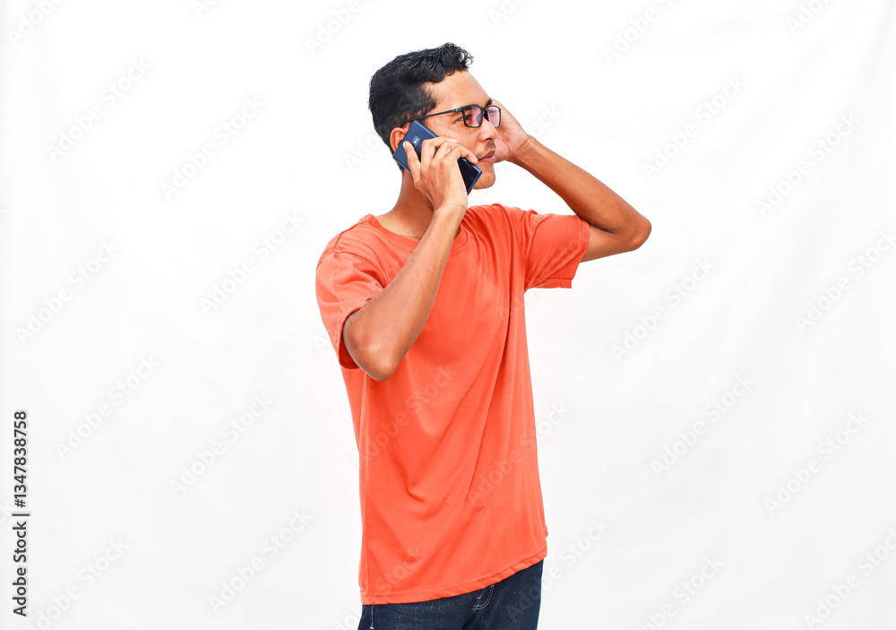 Young man in orange shirt engaged in a serious phone conversation on white backdrop Young man in orange shirt engaged in a serious phone conversation on white backdrop