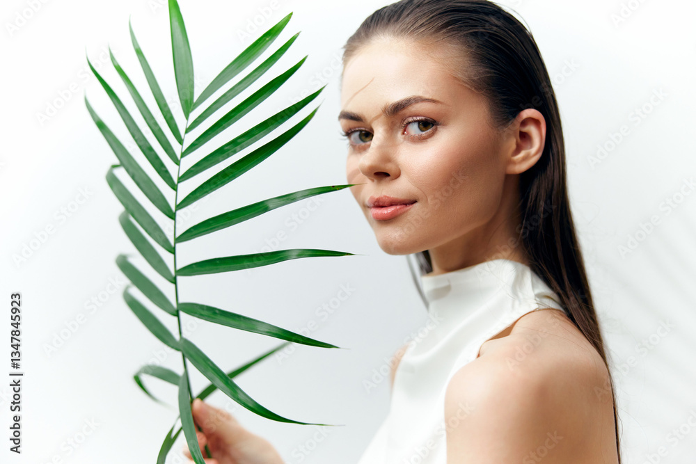 Beautiful young woman holding a green leaf, showcasing natural beauty and serenity in a bright, minimalist setting. Beautiful young woman holding a green leaf, showcasing natural beauty and serenity in a bright, minimalist setting.
