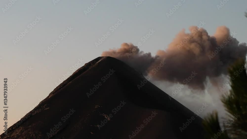 view of fuego volcano peak with smoke rising recent eruption (erupting volcanic ash lava fire) active seismic geothermal activity in antigua guatemala with trees (pyroclastic flow) hike acatenango