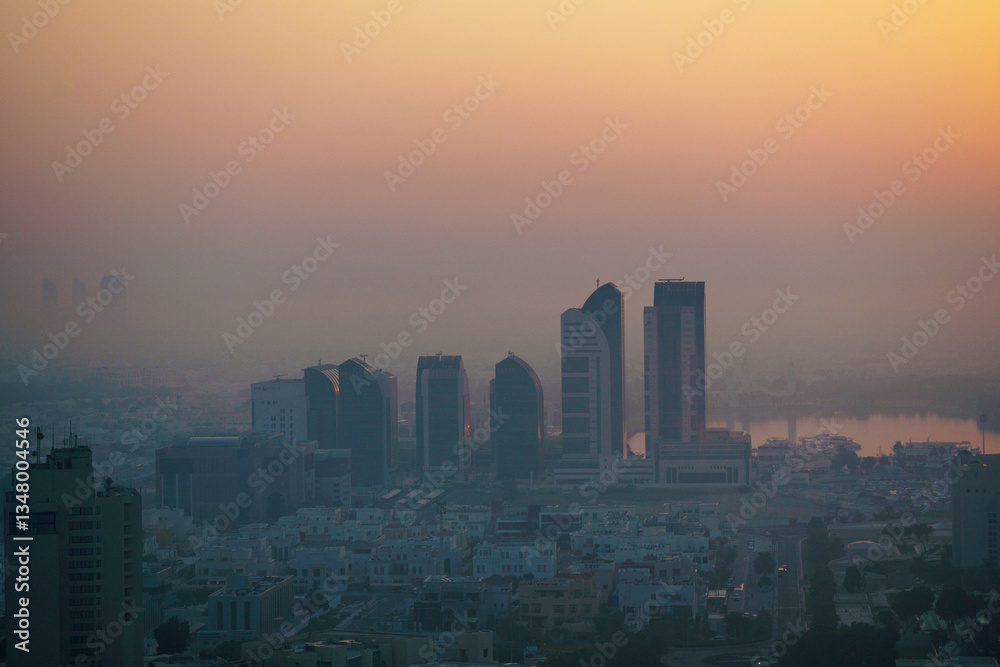 Fototapeta premium Aerial view of Abu Dhabi in the morning light, as the rising sun casts a golden glow over the city's modern skyline.