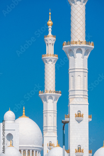 Close-up of the Sheikh Zayed Grand Mosque, showcasing its intricate white marble domes and elegant architectural details against a vivid blue sky. 