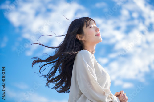 青空の下長い髪が風になびく日本人女性 Generative AI
